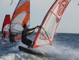 Drei Windsurfer fahren bei starkem Wind auf dem Meer.