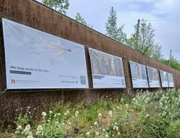 Große Plakat hängen an einer Mauer, darunter wachsen Pflanzen